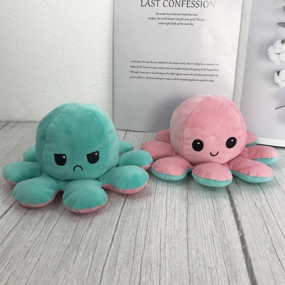 Two plush octopus toys, one teal and one pink, on a wooden surface with a book in the background.