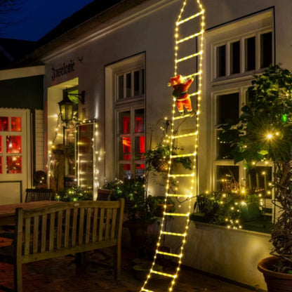 Decorative ladder with lights and a Santa Claus figure outside a building at night.