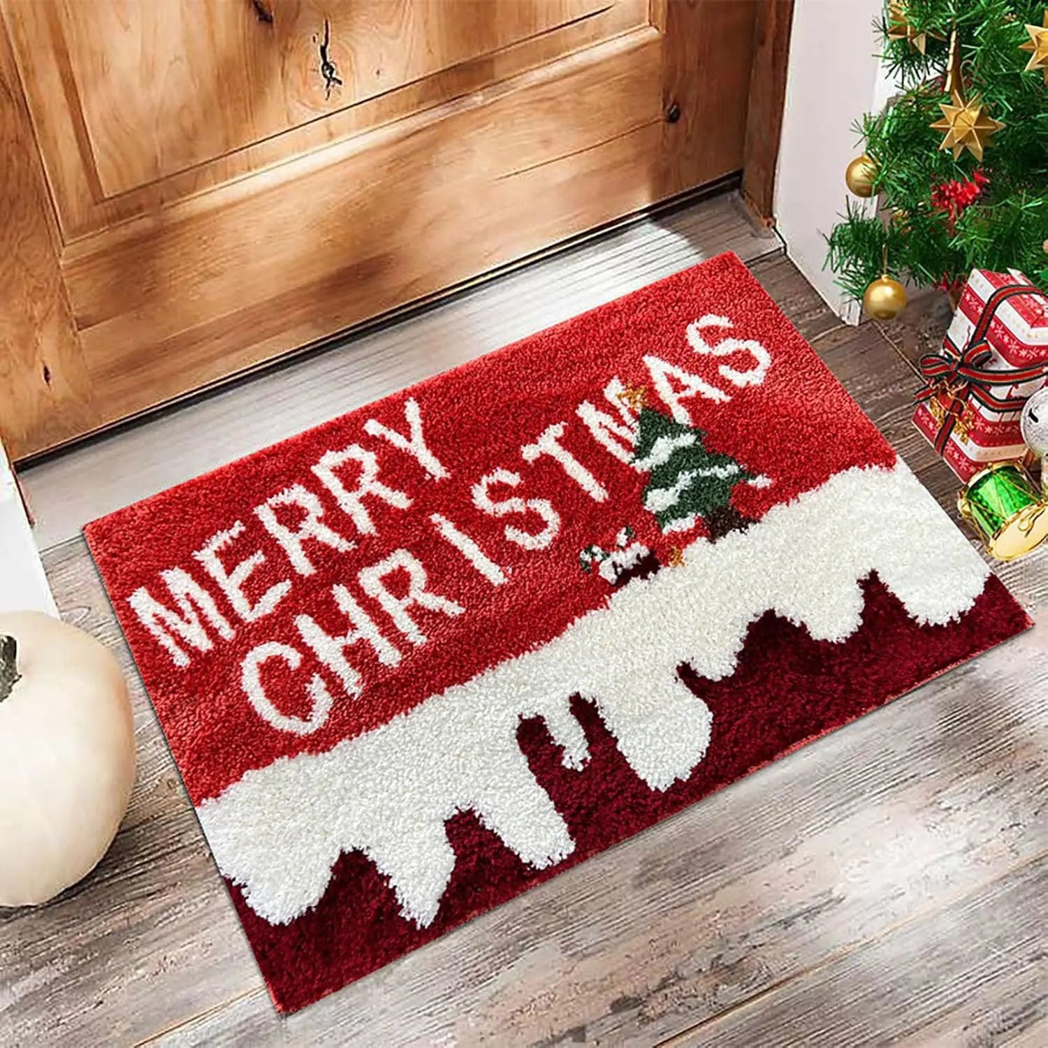 Red 'Merry Christmas' doormat on a wooden floor with a Christmas tree and presents in the background.